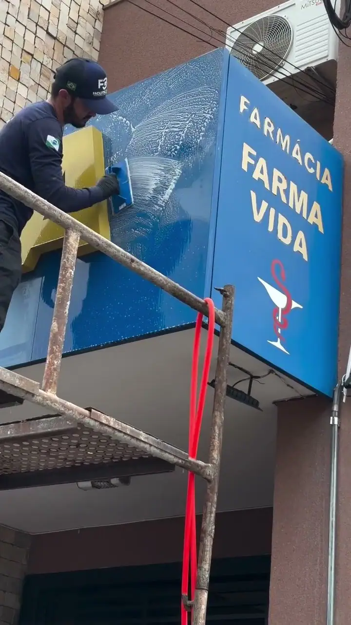 Profissional da Facilitta Clean aplicando produto no ACM azul do letreiro da farmácia