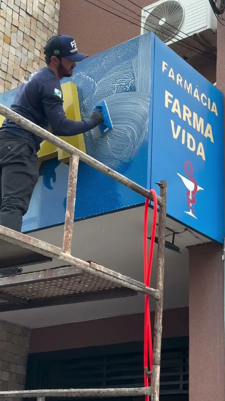 Profissional limpando o letreiro em ACM azul da Farmácia Farmavida