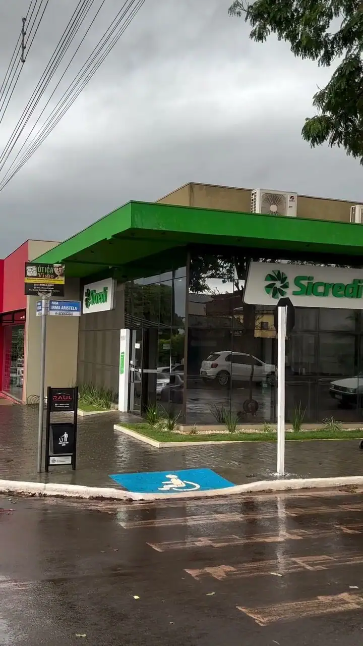 Agência Sicredi com fachada de vidro e a van da Facilitta Clean em dia de chuva