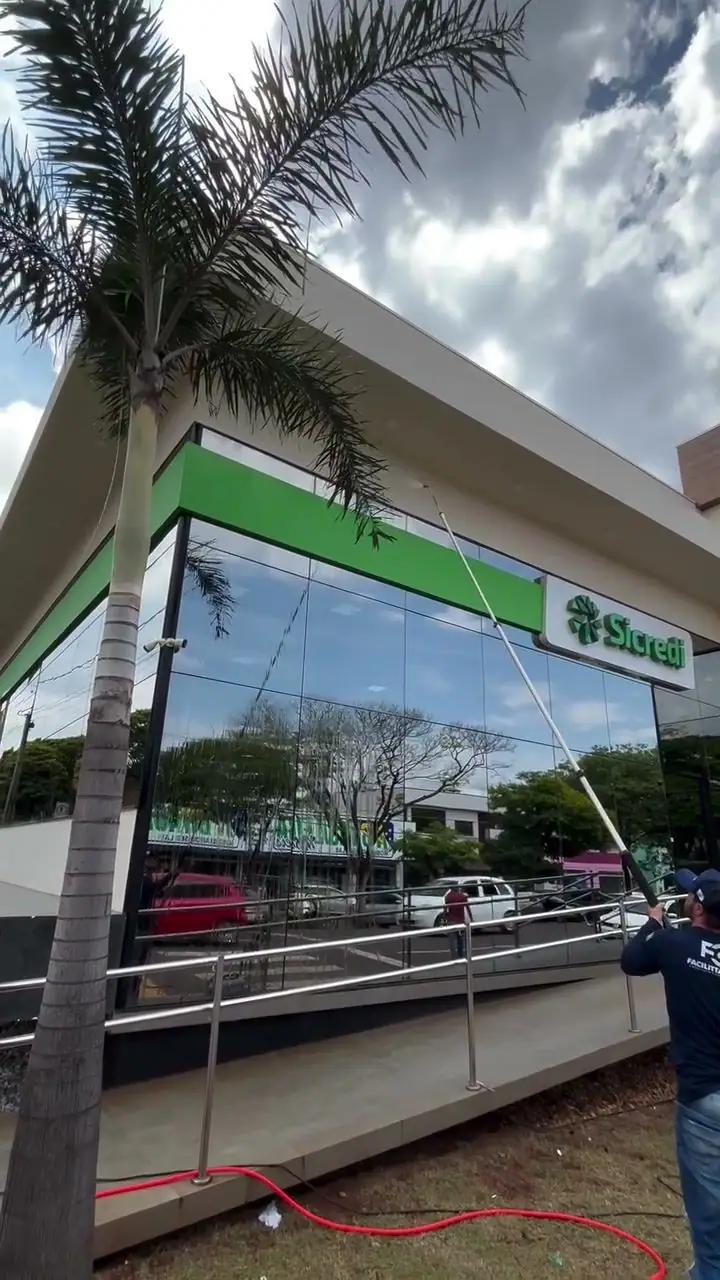 Profissional da Facilitta Clean limpando a fachada de vidro de uma agência Sicredi com haste telescópica